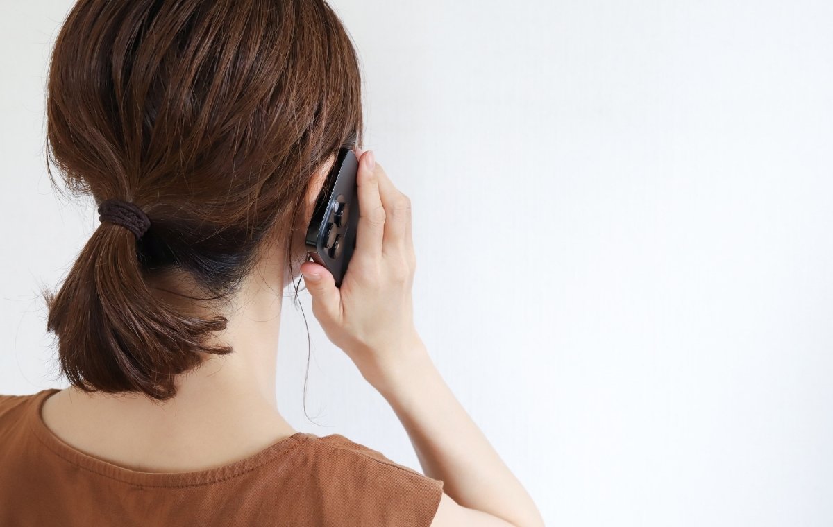 髪を結んだ女性がスマホで電話をかけている後ろ姿の写真