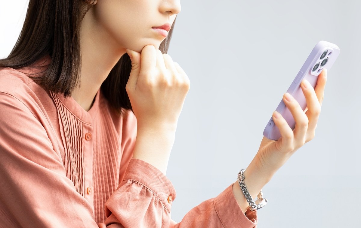 スマホを片手に悩む女性の写真