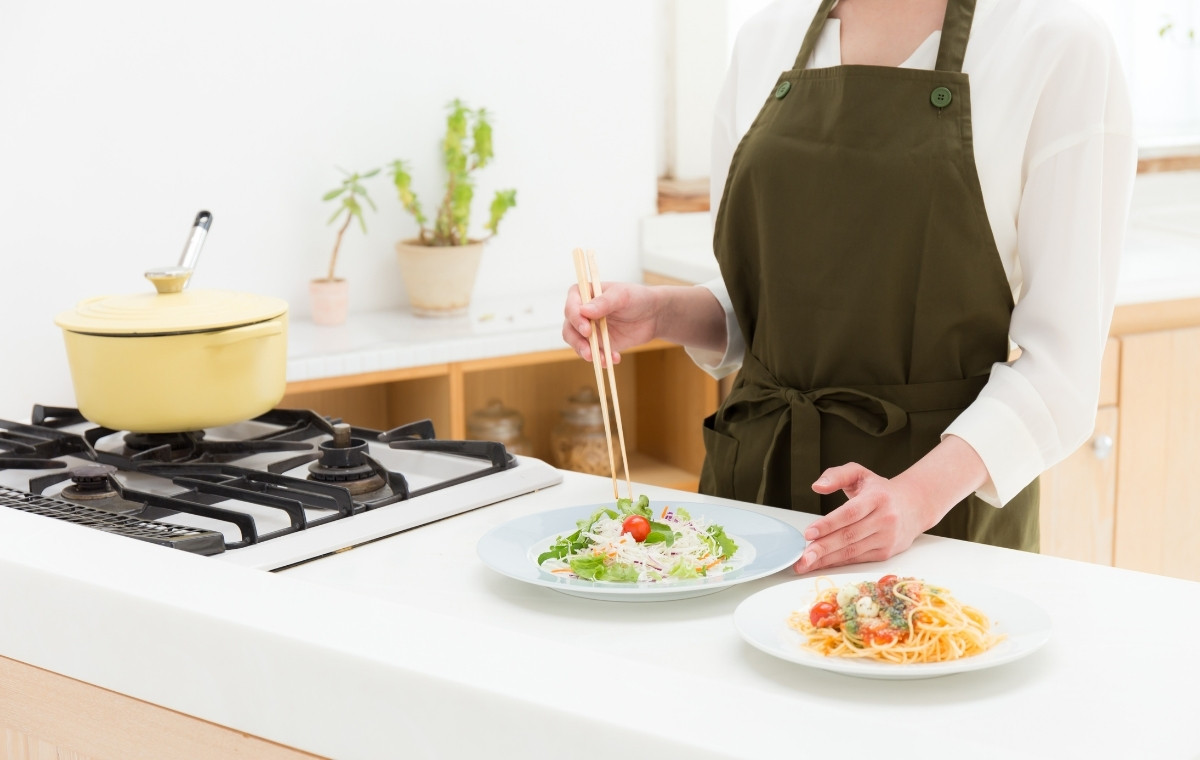 パスタとサラダを盛りつけているエプロン姿の女性の写真