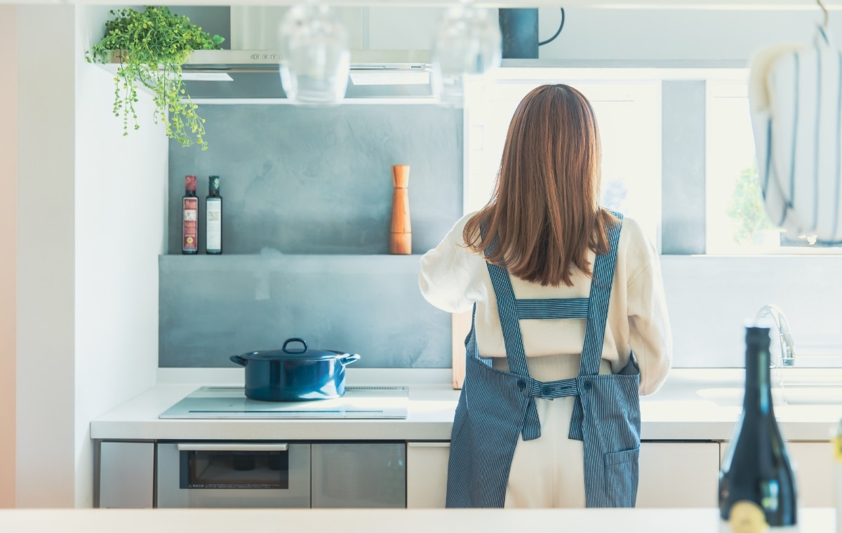 キッチンで作業するエプロン姿の女性の後姿の写真