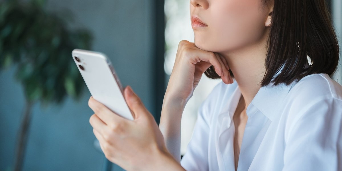 スマホを片手に考え事をする女性の写真