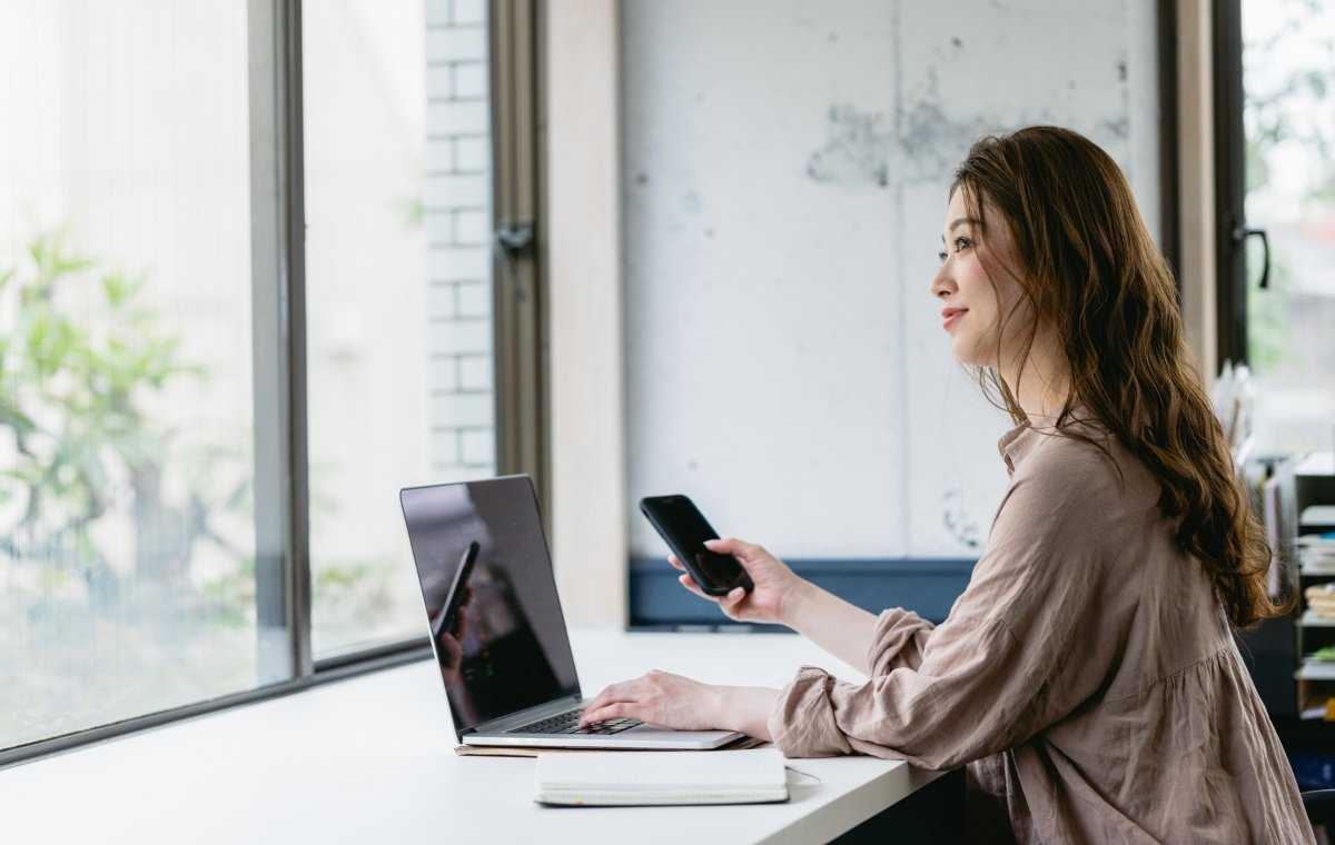 ノートパソコンとスマホを操作する女性の写真