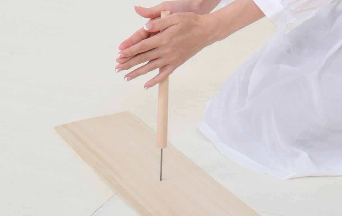 キリで板に穴を開けている女性の写真