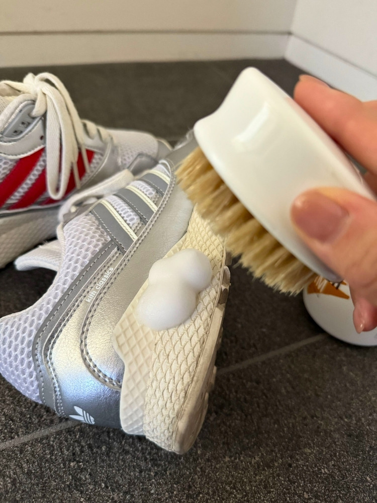 スニーカーのソールに泡を出し、ブラシを手に持っている写真
