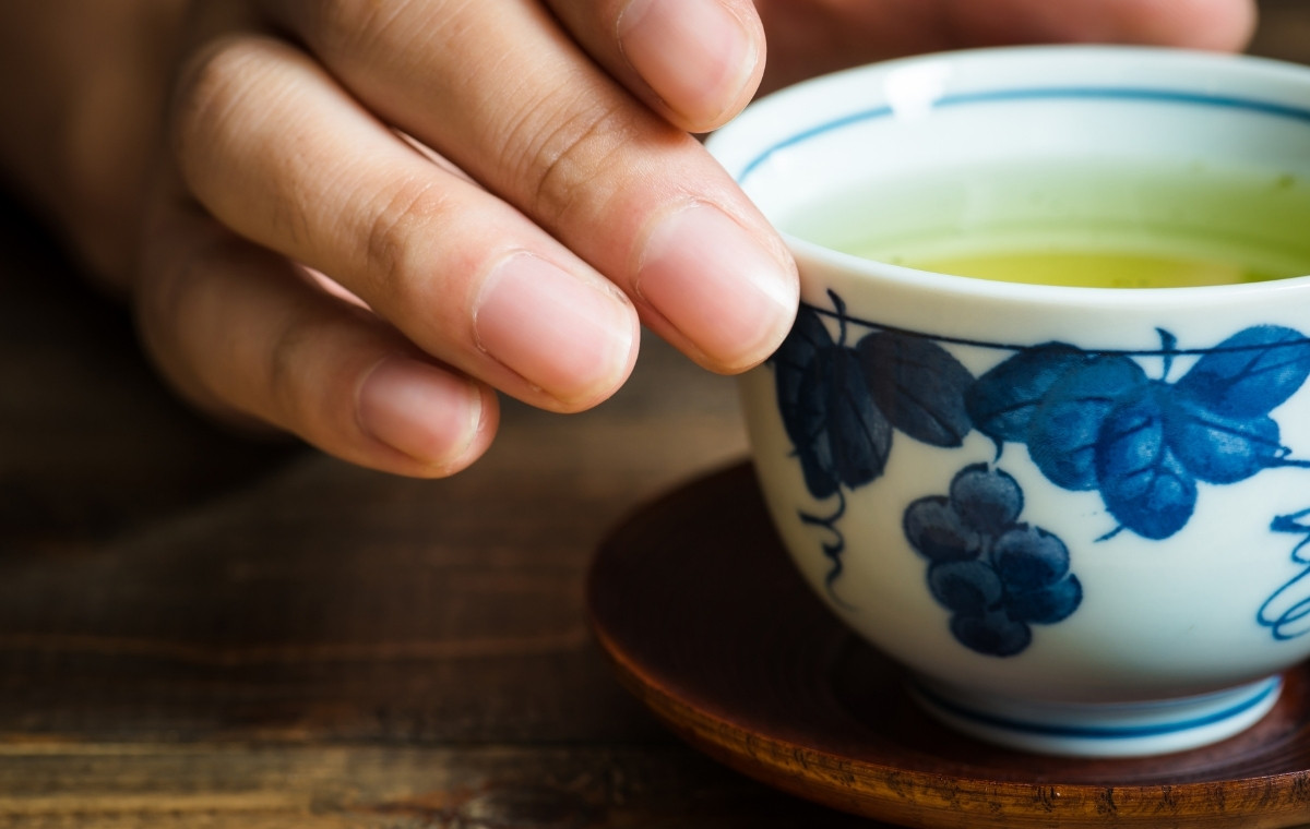 緑茶が入った湯飲みに手を添えている写真