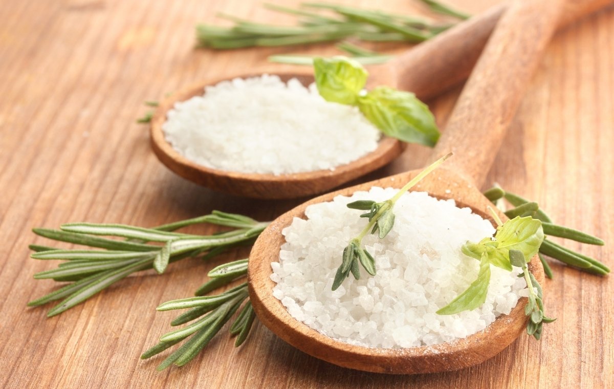 木のスプーンに盛られた塩のそばにローズマリーが置かれている写真