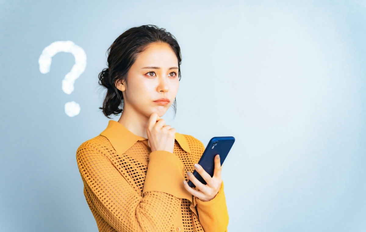 スマホを見てはてなマークを出して悩んでいる女性の写真