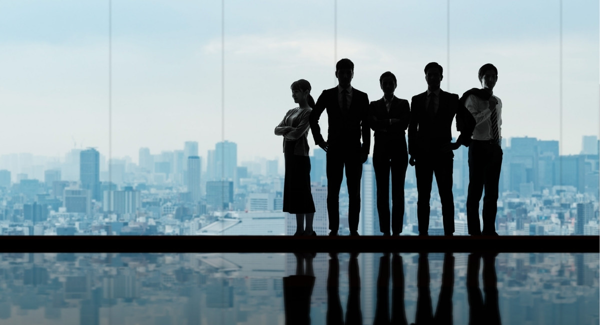 男女のビジネスパーソンが5人腕を組んで立っているシルエット
