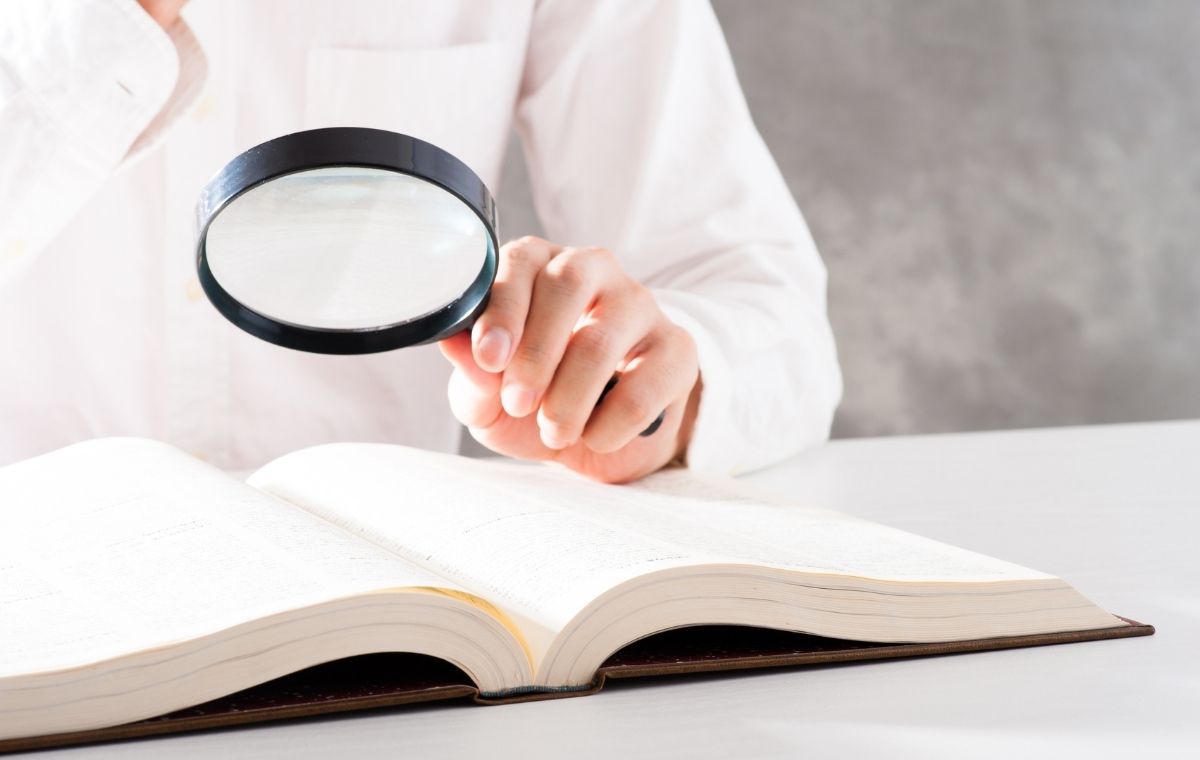 大きな辞書をルーペで見ている人の写真