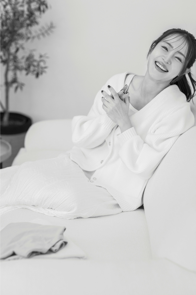 リラクシーなスタイルでソファに座るポニーテールの大沢さんの全身写真