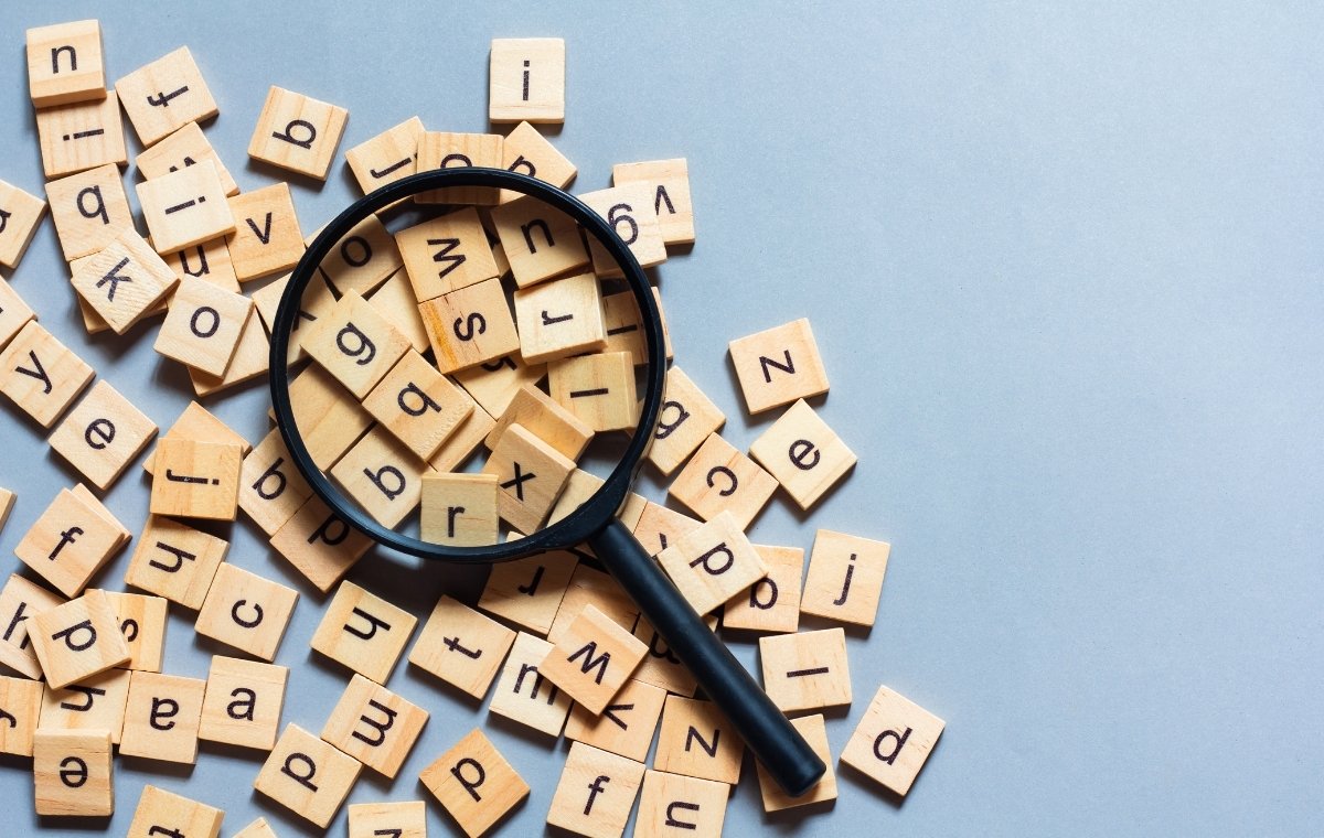 アルファベットが一文字ずつ書かれた木のチップが散らばっているうえにルーペが置かれている写真