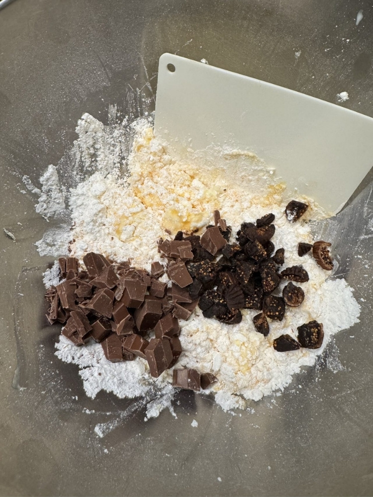 粉が入ったボウルにドライフルーツとチョコレートを入れている写真